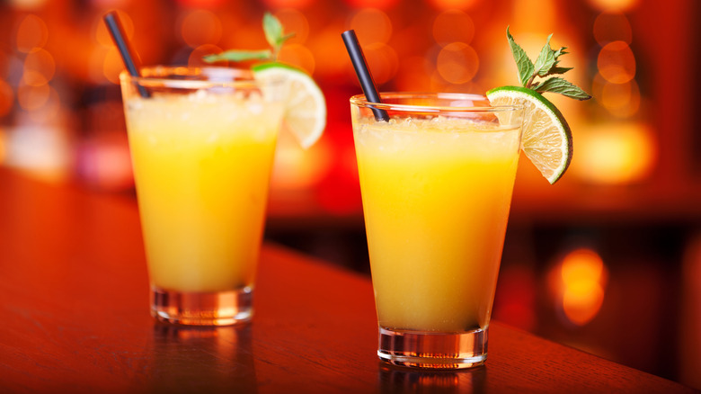 two Harvey Wallbanger cocktails on a bar with blurred yellow and orange lights in the background