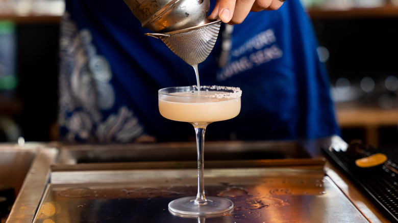 Person straining a drink into a glass at a bar