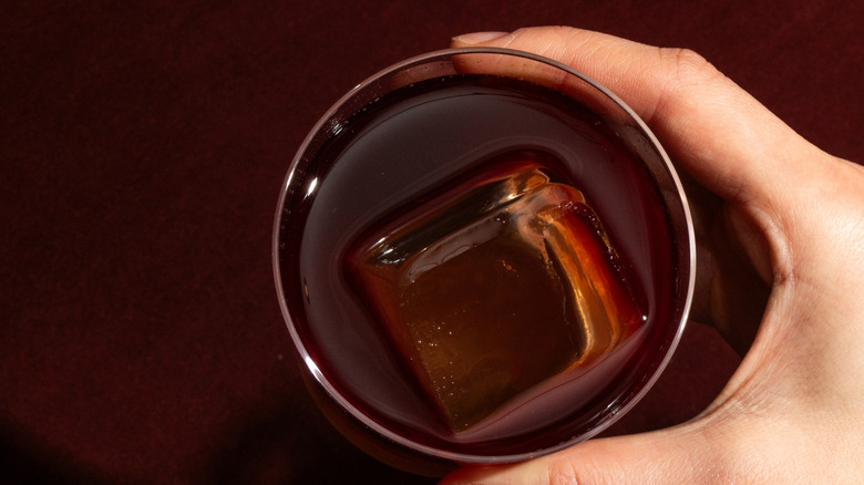 Close-up of a person's hand holding a Sazerac with a single iced cube as seen from above