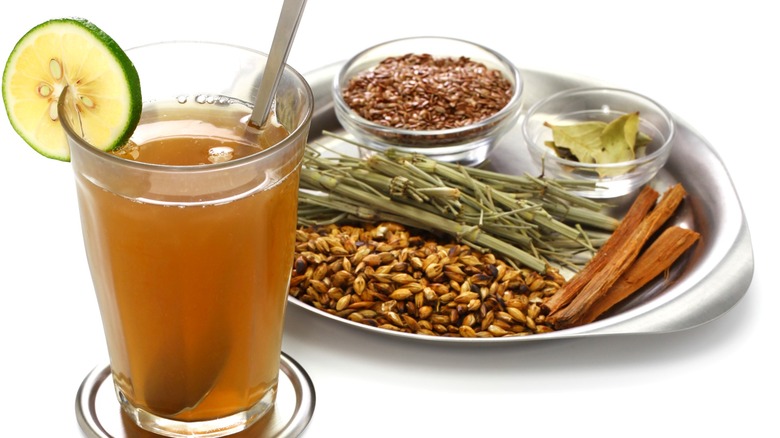 A glass of emoliente with the herbs used to make it in the background