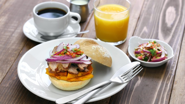 Pan con chicharrón sandwich on a plate with orange juice and coffee in the background