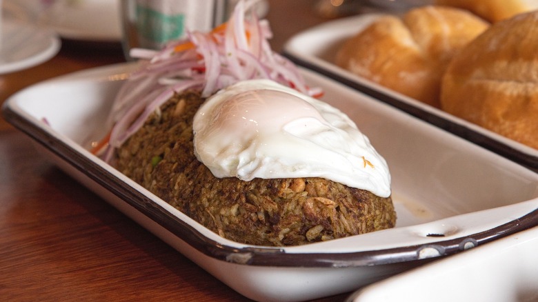 A plate of tacu tacu topped with an egg and salsa criolla