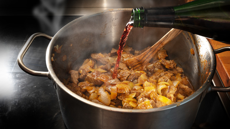 Red wine pouring into a pot with meat, onions and other ingredients