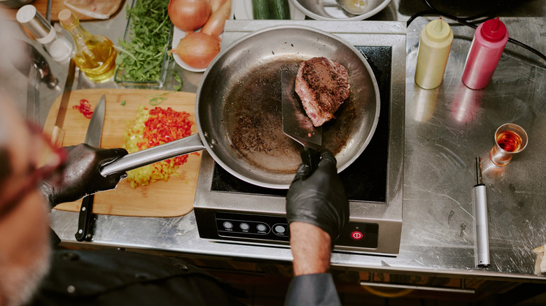 Person cooking steak in a pan with other ingredients and sauces and spices nearby
