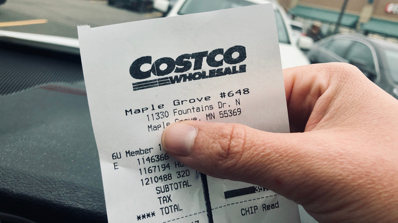 A hand holding a Costco receipt in a parking lot