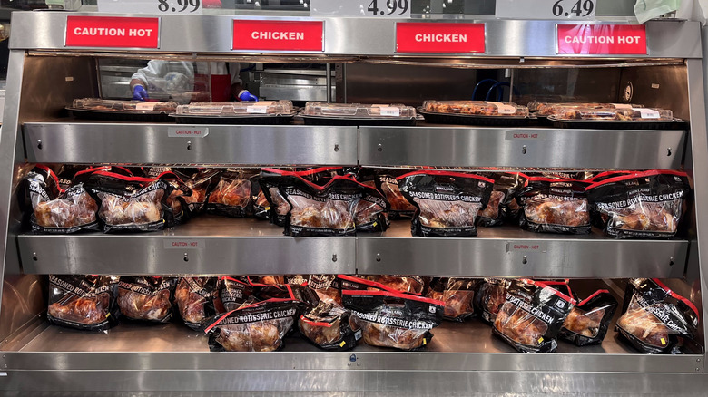 Plastic containers of Costco's rotisserie chicken on deli shelves
