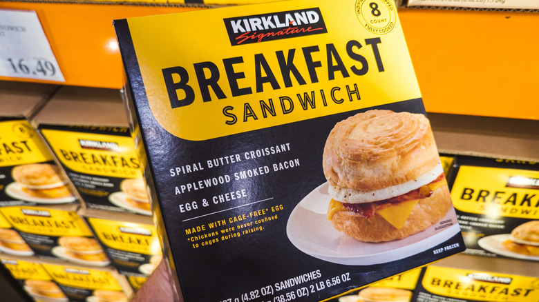 A person holding a box of Kirkland Signature Breakfast Sandwiches at a Costco warehouse