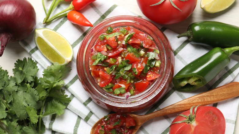 Overhead view of a jar of fresh salsa with ingredients used to make it