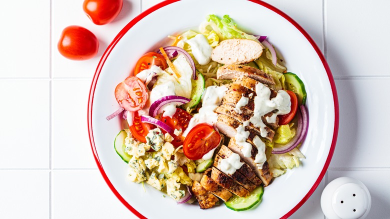 Overhead view of a white bowl full of salad with chicken and ranch dressing