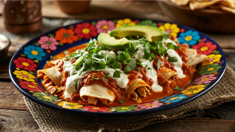 Dish of enchiladas smothered with crema, salsa, and sliced avocado