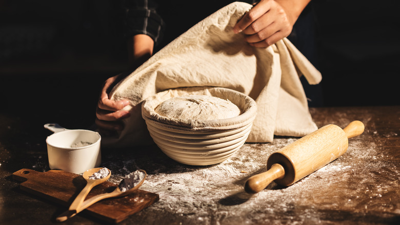 Hands covering bowl full of bread dough with a cloth