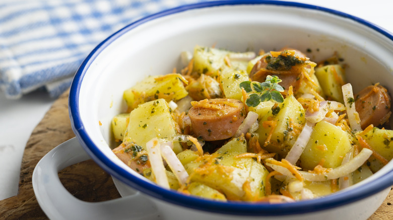 Potato salad with cut up sausages in a white bowl