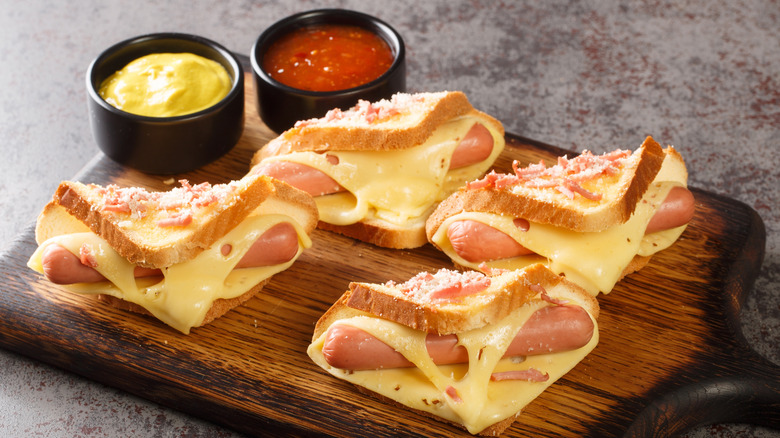 Vienna sausages on toasted white bread with melted cheese with dipping sauces on a wooden board