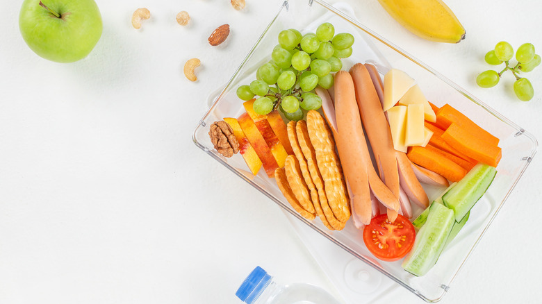 A platter of crackers, cheese, fruit, with sliced Vienna sausages
