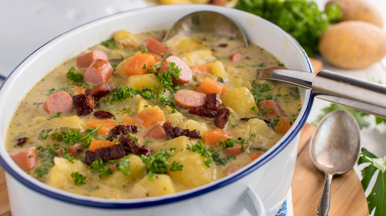 A bowl of soup consisting of a yellow broth, carrots, potatoes, Vienna sausages, and other veggies