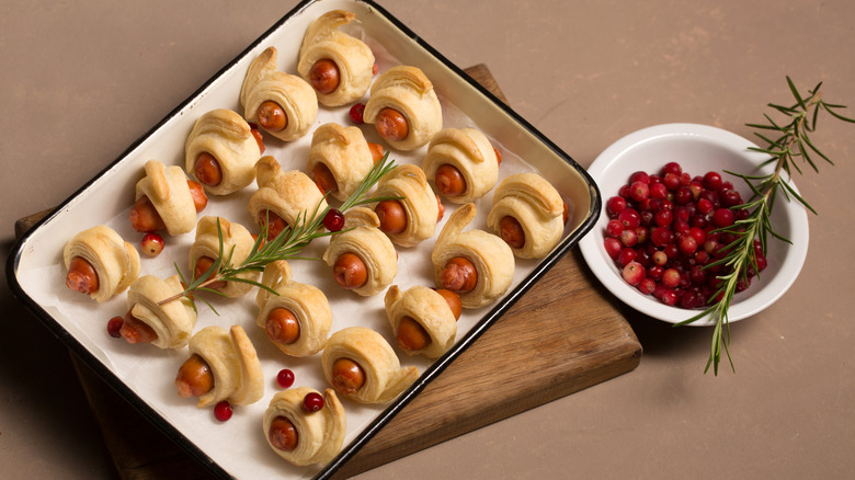 Pigs in a blankets on a tray next to a bowl of cranberries
