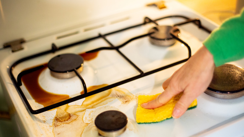 Person cleaning under stovetop with a sponge