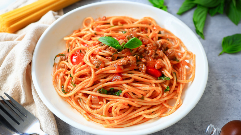 spagheti in tomatto sauce with minced ham in white bowl