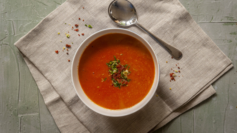 white bowl of bright red tomato soup with bacon and herb garnish