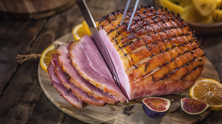glazed ham on a cutting board being carved with a knife
