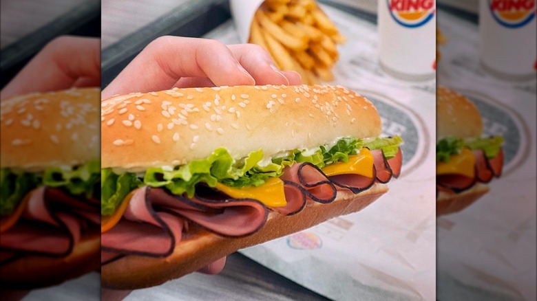 The Burger King Yumbo sandwich being held with a box of french fries and drink on a tray.