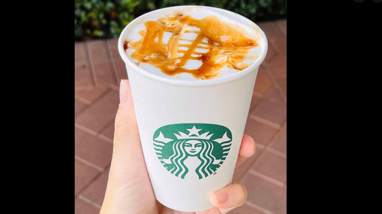 Apple crisp oatmilk macchiato in Starbucks cup surrounded by fall leaves