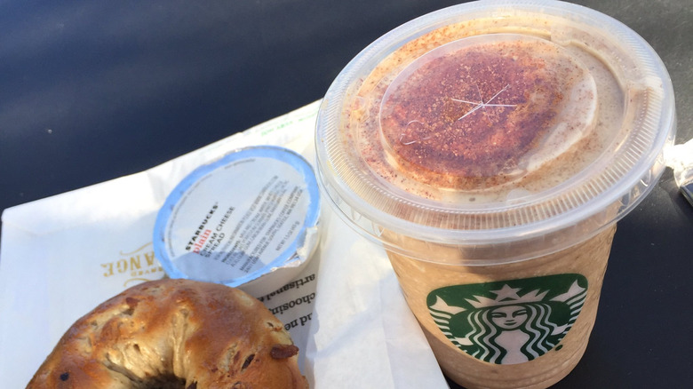 A chile mocha in a takeout cup next to a bagel from Starbucks