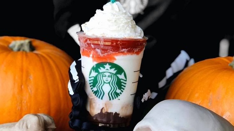 A Starbucks employee holding a Frappula Frappuccino surrounded by pumpkins and Halloween decorations