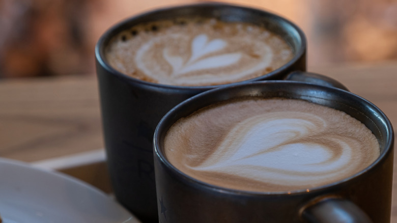 A close up of two black Starbucks mugs filled with creamy butterscotch latte with foam art on top