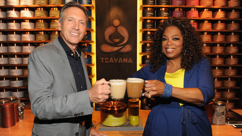 Oprah Winfrey and head of Teavana standing in front of a Teavana display holding glass mugs of Starbucks coffee