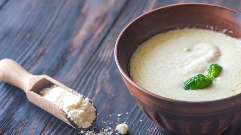 Bowl of Alfredo sauce with grated cheese spilling out of a wooden scoop