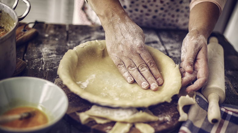 Person pressing pie dough with hands into tin