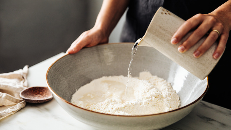 Person pouring water into bowl of flour