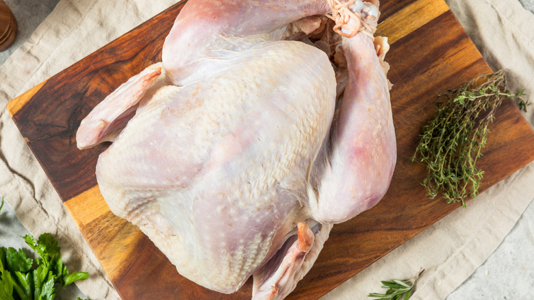 raw turkey on cutting board with herbs on the sides