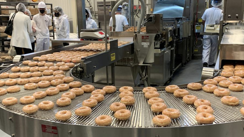 Krispy Kreme donuts roll along a conveyor belt.