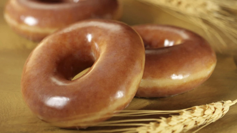Three Whole Wheat Glazed donuts from Krispy Kreme sit next to stalks of wheat.