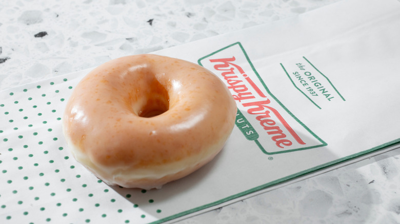 A Krispy Kreme Original Glazed donuts sits atop a Krispy Kreme bag.