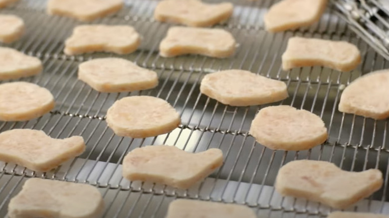 Raw Chicken McNuggets are carried on a conveyor belt.