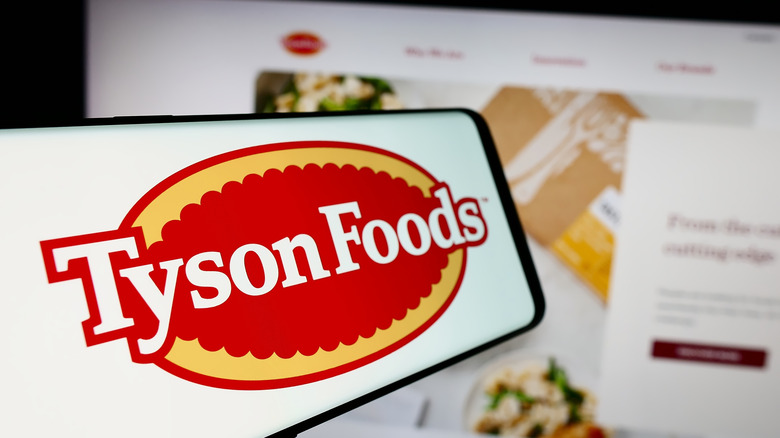 A phone screen featuring the Tyson Foods logo sits in front of a computer screen.