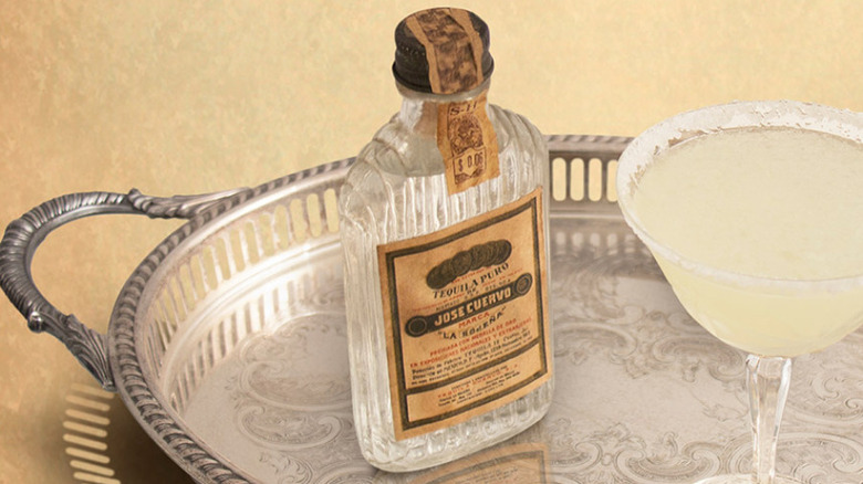 A bottles of Jose Cuervo tequila on a silver tray with a margarita