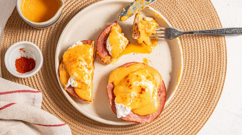 Partially eaten plate of eggs Benedict with hollandaise sauce and paprika in bowls on the side