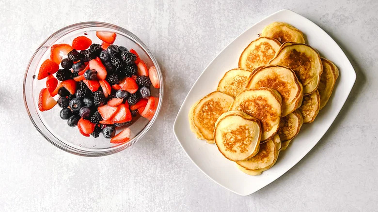 Bowl of macerated berries and rectangular white plate of fluffy lemon ricotta pancakes