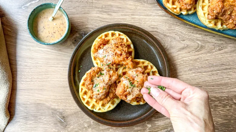 Person garnishing a plate of sweet and savory crispy buttermilk chicken and waffles