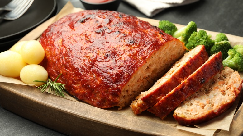 A turkey meatloaf with slices cut out on a platter with potatoes and broccoli
