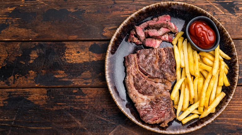 A plate of steak and fries with a side of ketchup