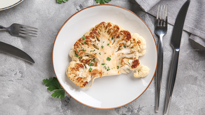 Cauliflower steak with charred surface, served on white plate