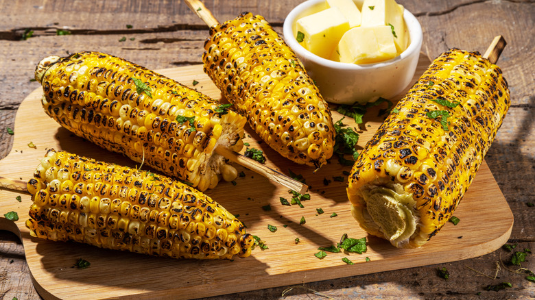 Corn on the cob with chargrill marks, served on a wooden board with butter