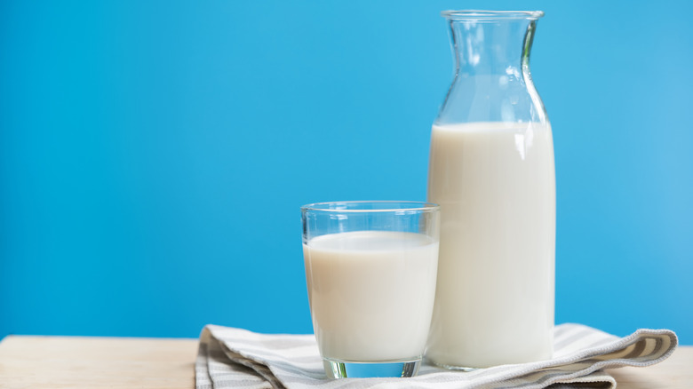 a glass and carafe of milk with blue background