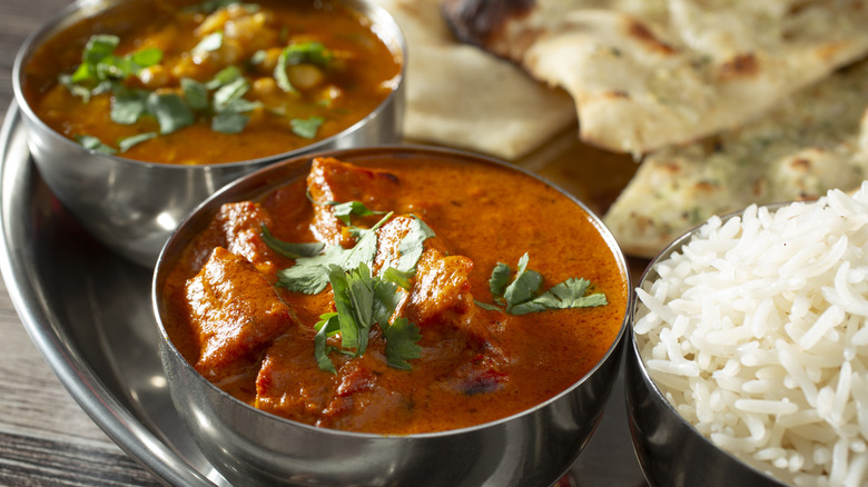Two bowls of curry and rice with naan bread