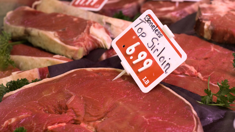 Meat case with steaks and greens with a price labeled on a small sign stuck into a boneless top sirloin steak